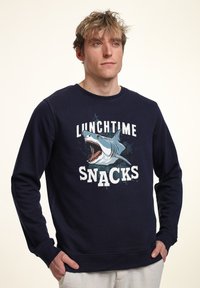 Sudadera de algodón en color azul marino con un gráfico de un tiburón y el texto "SNACKS DE HORA DEL ALMUERZO", con puños y dobladillo acanalados. Corte casual.