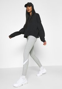 Sweatshirt nero corto, leggins grigi con accenti bianchi e sneakers bianche. Il tessuto sembra morbido con una vestibilità comoda e maniche oversize.