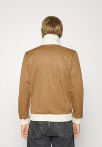 Brun jacka med en slät textur, med en vit ribbad krage och manschetter, midjelång design och subtila sömnadsdetaljer.