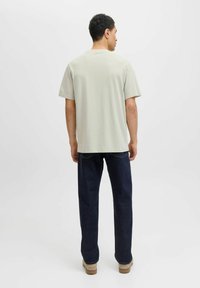 Tricou din bumbac gri deschis, cu o croială relaxată, mâneci scurte, gât rotund, asortat cu blugi drepti de culoare bleumarin și pantofi bej.
