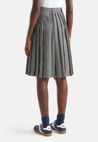 Šedá a bílá kostkovaná plisovaná sukně s vysokým pasem. V kombinaci s námořnickými teniskami a modrými ponožkami, které vykazují uvolněný střih.