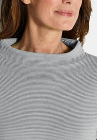 Lichtgrijze, textuurvolle top met een hoge, ribbelige halslijn. Glad materiaal met subtiele horizontale lijnen en een relaxte pasvorm rond de schouders.
