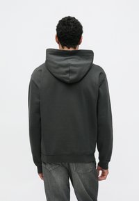 Temno siva jopa s kapuco, prostorno kapuco, rebrastimi manšetami in spodnjim robom, narejena iz mehkega, teksturiranega blaga. Nošena čez kavbojke z vidnimi zadnjimi žepi.