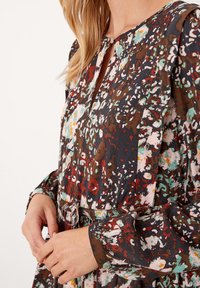 Blommig klänning med mörk bakgrund och färgglada mönster i röd, grön och vit, nyckelhålsringning, långa ärmar och ett knytbälte.