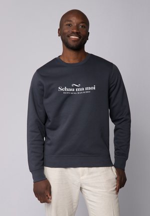 Donkergrijze sweatshirt met ronde hals, voorzien van witte tekst "Schau ma moi" en "DANN SENG MAS SCHÓ!" op de voorkant. Zachte stoffen textuur.