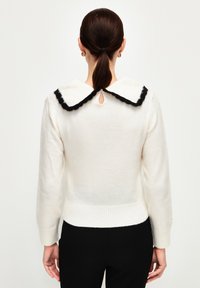 Pull en tricot blanc avec un col noir à bord festonné, un détail en trou de clé à l'arrière, et des finitions côtelées à l'hem et aux poignets pour un aspect ajusté.