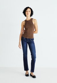 Bruine geribbelde tanktop met een ronde halslijn en zwart logo, gecombineerd met rechttoe rechtaan donkerblauwe jeans en zwarte ballerina's.