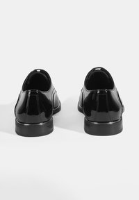 Schwarze Lacklederschuhe mit einer glatten, glänzenden Oberfläche, abgerundetem Zehenbereich und einem kleinen, stabilen Absatz. Minimalistisches Design.