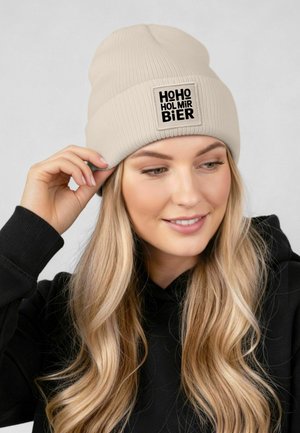 Cream-colored knitted beanie with a ribbed texture and a square black logo patch reading "HOHO HOLMIR BIER."