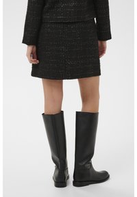 Černá sukně z tvídu s texturovanou tkaninou, spárovaná s černými kozačkami ke kolenům z hladké kůže s minimálními švy.