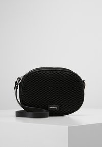 Zwarte mesh schoudertas met een ronde vorm, gladdetailing, ritssluiting en een verstelbare strap. Logo aan de voorkant weergegeven.