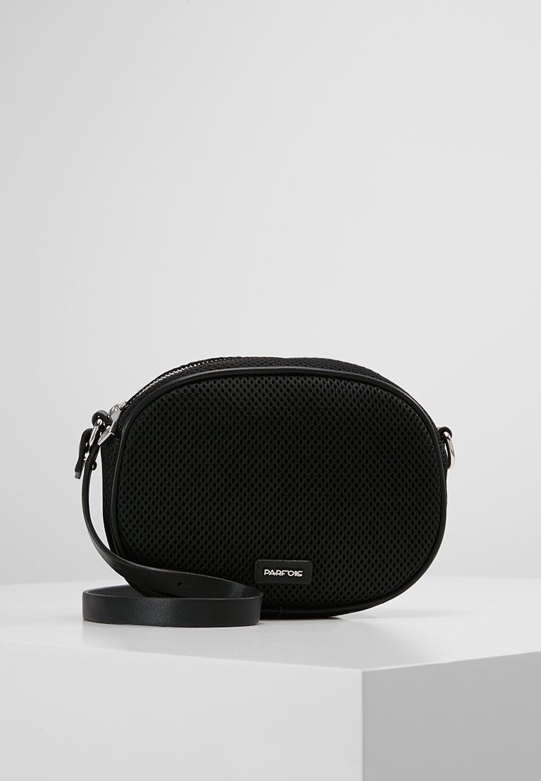 Zwarte mesh schoudertas met een ronde vorm, gladdetailing, ritssluiting en een verstelbare strap. Logo aan de voorkant weergegeven.