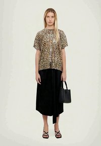 Zlatni in črni bleščičasti top s kratkimi rokavi, usklajen s črno dolgo krilo. Model drži majhno črno torbico in nosi črne sandale s trakovi.