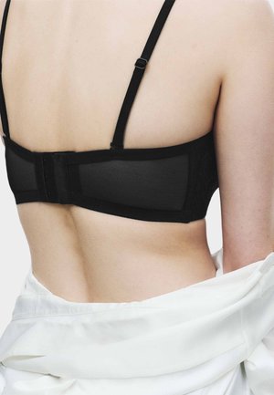 Bagside af en person, der bærer en sort bh med justerbare stropper og et hvidt stykke tøj draperet omkring taljen.