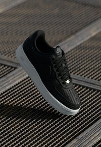 Crni Nike Air Force 1 tenisice, s teksturiranom gornjom površinom, vezanjem na vezice i bijelim gumeno potplat, s diskretnim logotipom na jeziku.