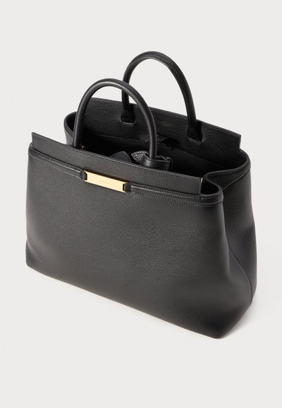 Musta nahkakäsilaukku, jossa on jämäkkä muoto, kaksinkertaiset kahvat ja kultasävyinen metalliaksentti etupuolella. Kenttä kuviointi pinnassa.