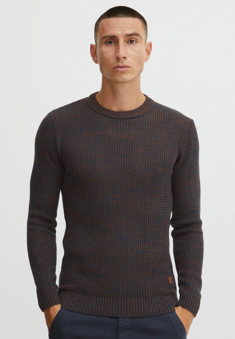 Dark knit sweater with a round neck, featuring a textured pattern in dark blue and brown. Ribbed cuffs and waistband. Minimalist logo detail.