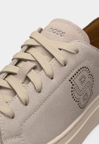 Baskets en daim beige avec lacets tressés, le mot "BOSS" embossé sur la languette et logo "B" perforé sur le côté.