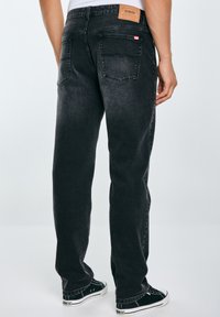 Jeans in denim nero con fit dritto, caratterizzati da una patch in pelle nella vita, due tasche posteriori e dettagli di cucitura minimal.
