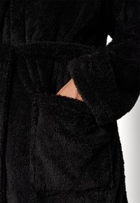 Black fluffy bathrobe featuring a textured fabric, a tie waist, and large front pockets. The sleeves are wide and slightly rolled.