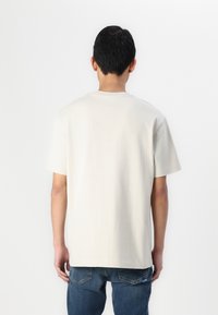 Lys beige kortærmet t-shirt med rund hals, glat tekstur og afslappet pasform, parret med mørkeblå jeans.