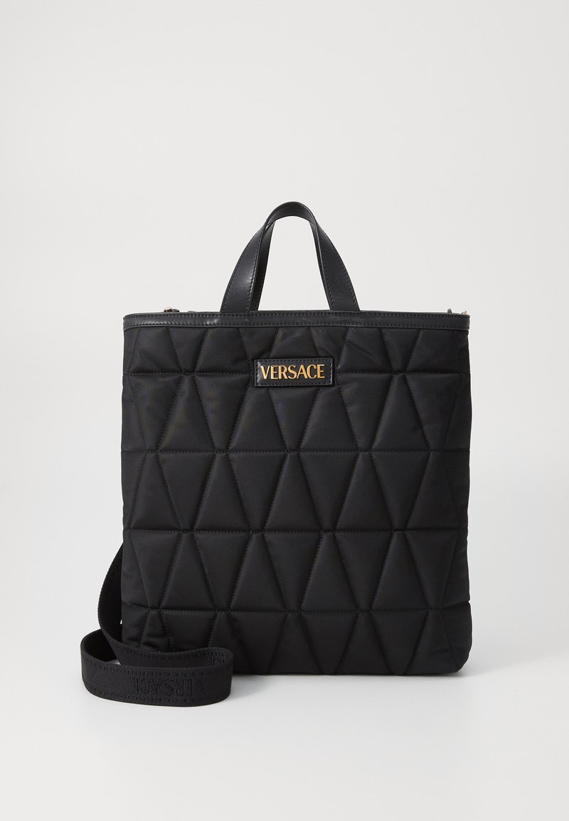 Saco tote de nylon acolchoado preto com padrões triangulares, detalhes em pele, alças superiores e uma alça destacável com o logótipo dourado da Versace.