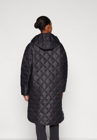 Long black quilted puffer coat with a hood, featuring a diamond pattern, made of a shiny, smooth material, extending to mid-calf.
