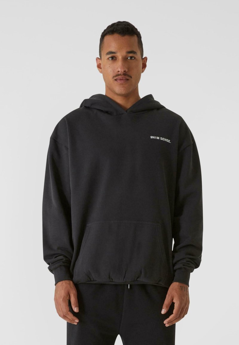 Black hoodie with a front kangaroo pocket, long sleeves, and a drawstring hood. Features "9N1M SENSE." in white text on the chest.
