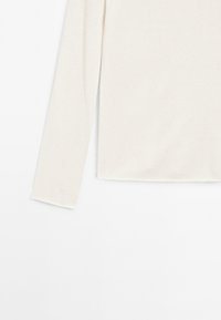 Pitkähihainen paita pehmeästä, kermaan vivahtavasta kankaasta. Siinä on rento istuvuus ja pyöristetty helma, minimaalisilla saumoilla eikä näkyviä kiinnityksiä.