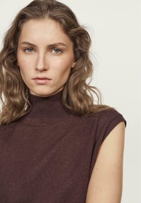 Top senza maniche a collo alto, di colore marrone scuro, con una vestibilità attillata, caratterizzato da un design a coste e un tessuto morbido e testurizzato.