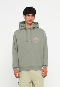 Groene hoodie met een trekkoord, een voorzak en een roze cirkelvormig logo op de borst. Glad materiaal, casual pasvorm, ribgebreide manchetten en zoom.