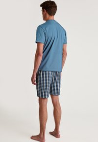 Men's light blue cotton T-shirt, paired with navy and white checkered shorts. The fabric is smooth, with a relaxed fit and short sleeves.