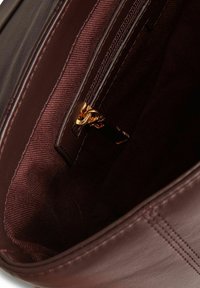 L'interno della borsa in pelle marrone presenta una tasca con cerniera con ferrature color oro e una fodera testurizzata in una ricca tonalità borgogna.