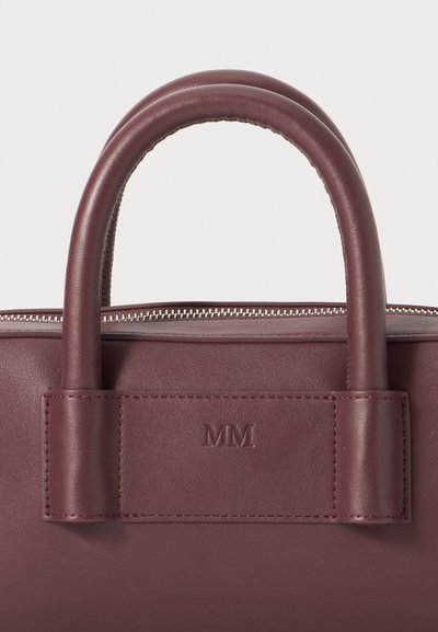 Μπορντό δερμάτινη τσάντα χεριού με φερμουάρ, στρογγυλές λαβές και διακριτικό ανάγλυφο λογότυπο "MM" σε κάθετη λωρίδα.