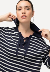 Navy- und weiß gestreifter Pullover mit Schnürkragen und oversized Kragen, aus Strickstoff, versehen mit großen Hoop-Ohrringen.