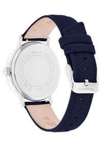 Marineblaue Stoffuhr mit Gehäuse und Schnalle aus Edelstahl. Verfügt über eine beigefarbene Lederunterseite und eine eingravierte Markenbezeichnung auf der Rückseite.