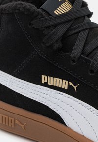 Čern�é semišové tenisky s bílým koženým pruhem, s texturovanými tkaničkami, zlatým logem Puma a hnědou gumovou podrážkou.