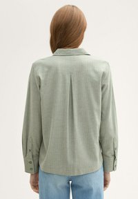 Zelená košile s dlouhým rukávem a límečkem, s rozparkem na zadní straně a knoflíkovými manžetami; vyrobená z texturované látky s jemným vzorem.