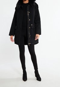 Sort isoleret parka med en falsk pelskrave, med lynlås lukning, sidelommer og gyldne detaljer. Båret med sorte leggings og ankelstøvler.