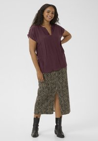 Maroon short-sleeve top with a v-neck, paired with a long, patterned, beige and black skirt featuring a side slit, and black ankle boots.