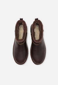 Botas tobilleras de cuero marrón con un suave forro de piel sintética, cremalleras laterales y un detalle de costura a lo largo del cuello y la suela.