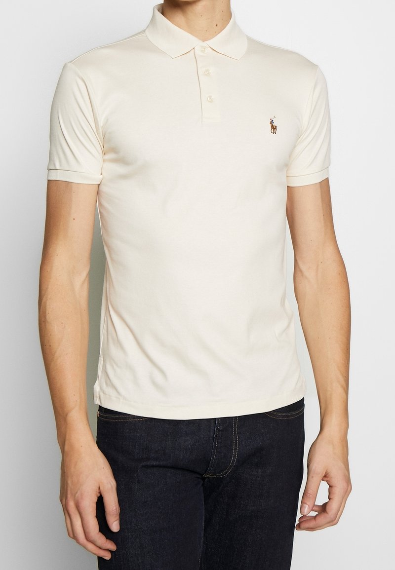 Polo à manches courtes de couleur crème, en coton, doté d'une patte de boutonnage à trois boutons et d'un petit logo brodé sur le côté gauche de la poitrine.