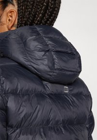 Marineblaue Steppjacke mit Kapuze, ausgestattet mit einem gesteppten Design und glänzender Textur. Ein kleines Logo-Detail über der Schulter verleiht zusätzlichen Stil.