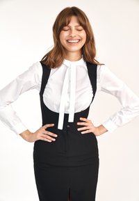 Czarna dopasowana sukienka z bocznym rozcięciem, z biał�ą koszulą zapinaną na guziki pod przypominającą kamizelkę górną częścią oraz kokardą przy szyi.