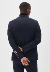 Marineblazer mit Reverskragen und Ein-Knopf-Verschluss, aus strukturiertem Stoff, mit drei Knöpfen an jedem Ärmel. Das Modell steht mit verschränkten Armen.