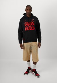 Felpa nera con grafica rossa "Chicago Bulls", pantaloni corti in denim beige e sneakers nere/rosse. Tessuto a trama con vestibilità comoda.
