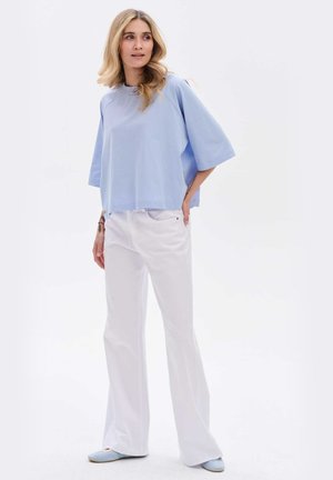 Lichtblauwe oversized top met brede mouwen, gecombineerd met witte wijde broekspijpen. Schoeisel heeft lichtblauwe accenten. Soepele textuur.