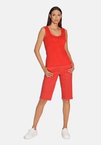 Rode tanktop en shorts tot de knie in een casual pasvorm. Gemaakt van zachte stof, met een ronde halslijn en een rafelige zoom. Witte sneakers.