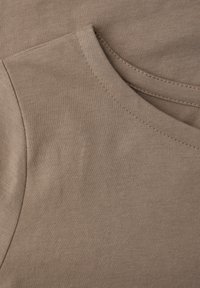 Gros plan sur un tissu en coton beige montrant l'encolure ronde cousue et la couture d'épaule d'un t-shirt uni.