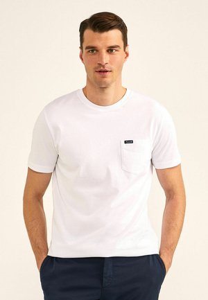 Witte katoenen t-shirt met een ronde hals, korte mouwen en een borstzak met een zwart etiket. Zachte textuur met een casual pasvorm.